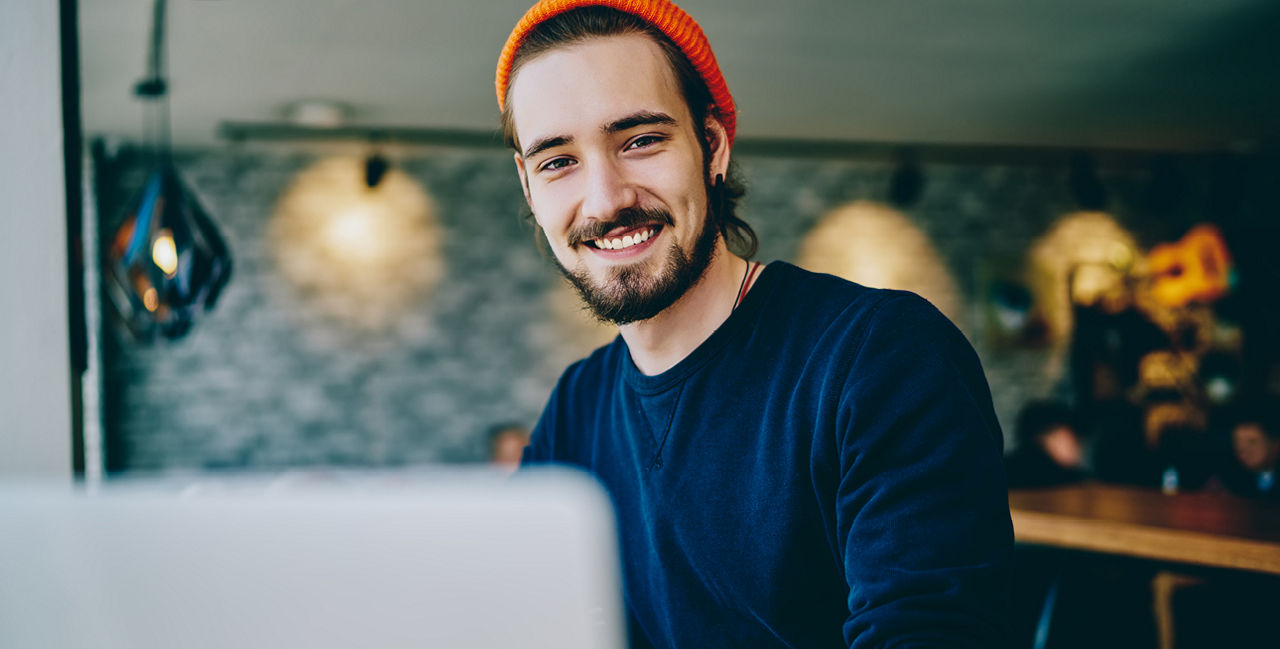 Junger Mann mit orangener Mütze vor Laptop