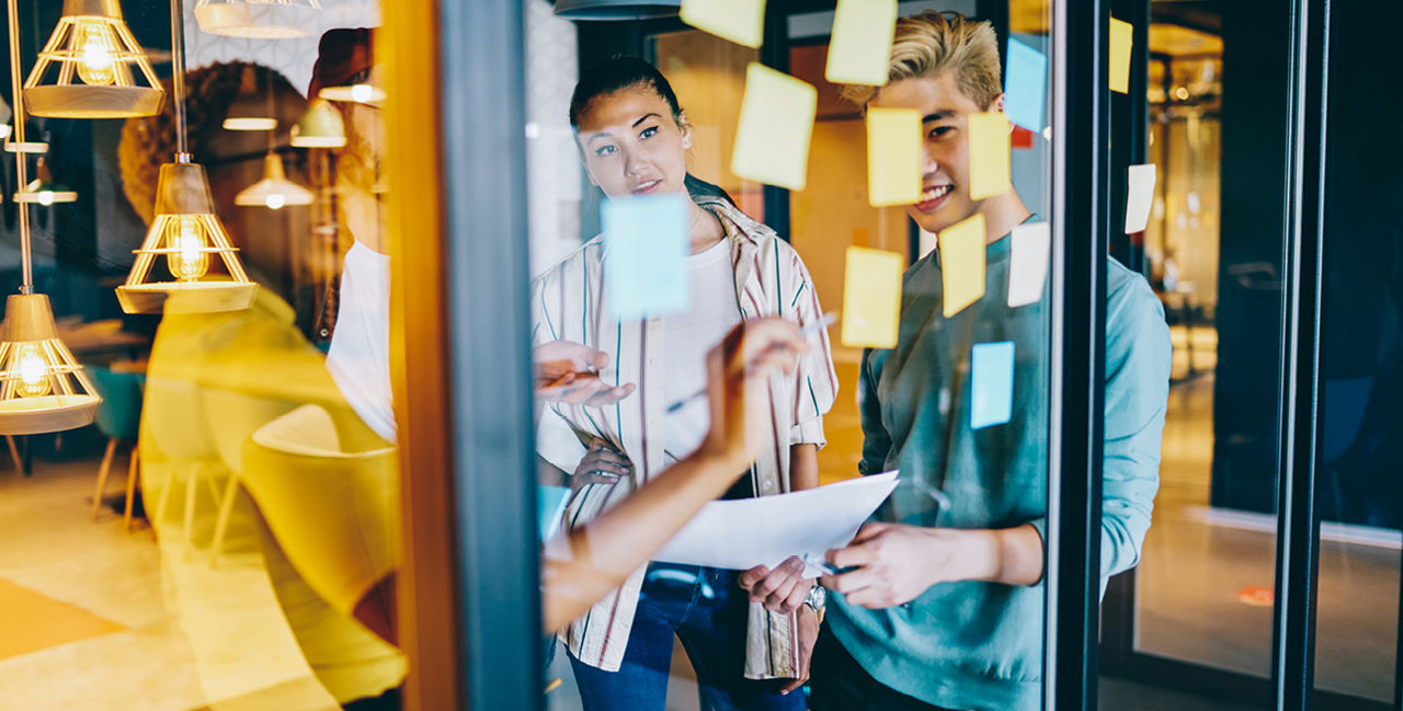 Gruppe junger Personen in einer Besprechung vor Glaswand mit Haftnotizen