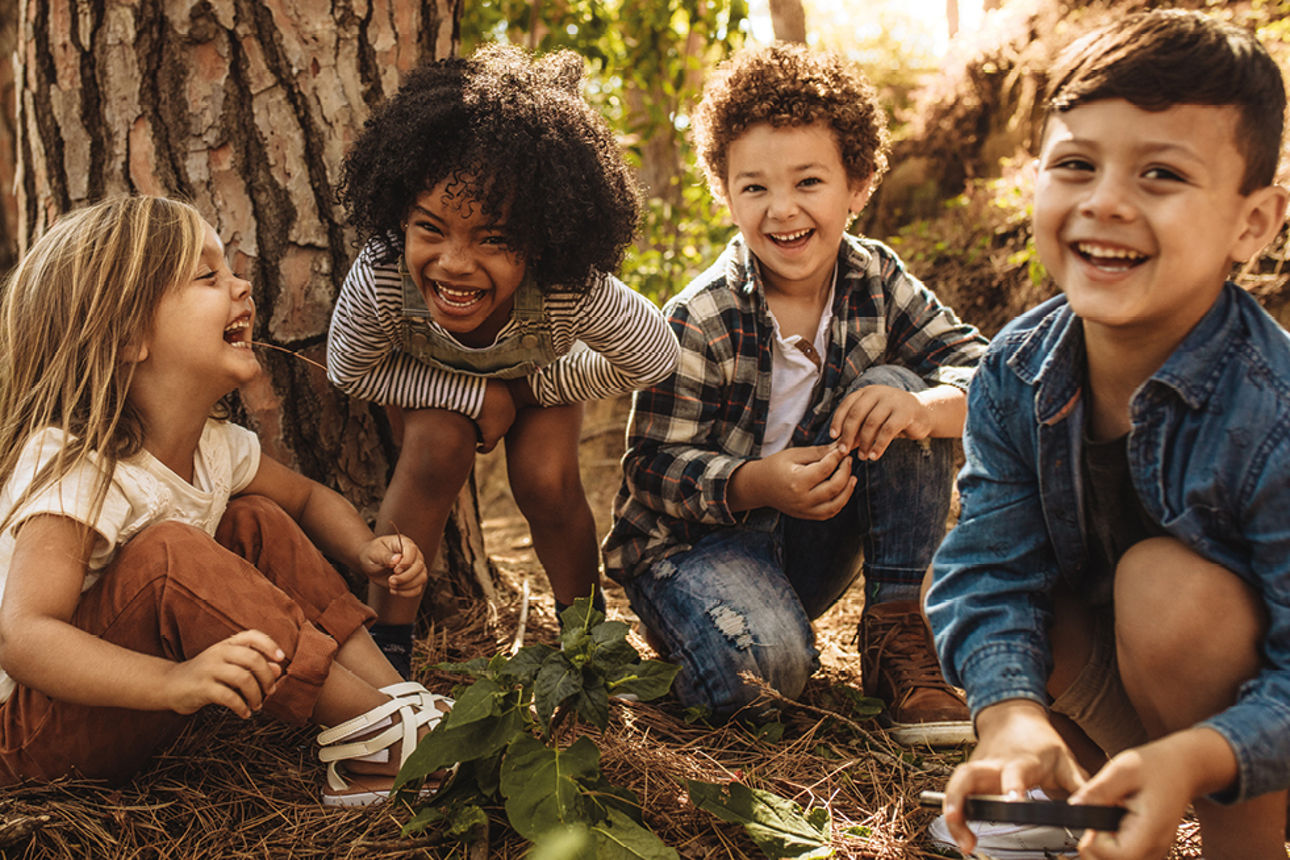 Vier Kinder sitzen in einem Wald auf dem Boden.