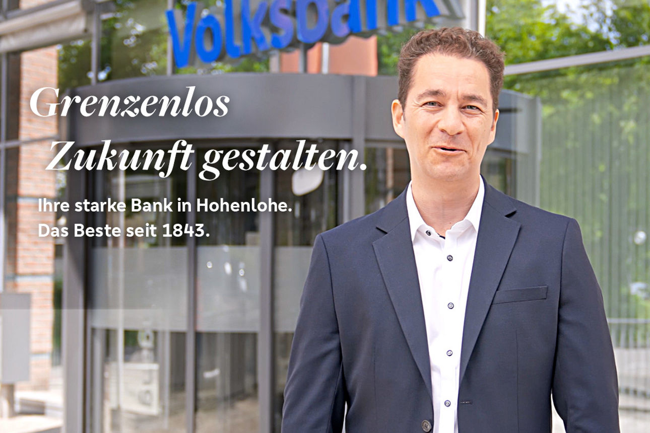 Bänker der vor Haupteingang der Volksbank Hohenlohe eG in Künzelsau steht mit der Überschrift Grenzenlos Zukunft gestalten