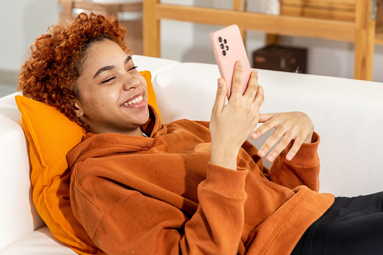Junge Person liegt mit Handy auf einem Sofa