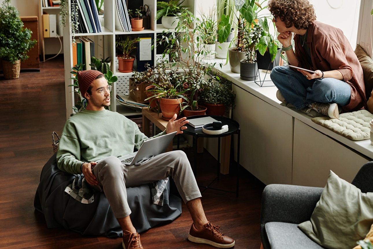 Mann im Sitzsack mit Laptop und Frau mit Tablet auf Fensterbank sitzend