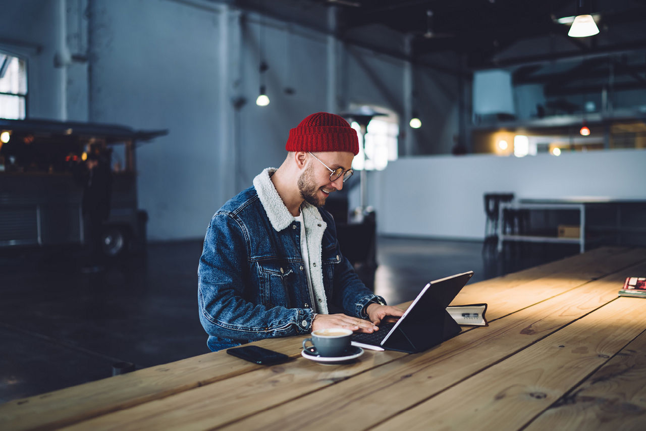 Person mit Laptop und Kaffee an langem Holztisch sitzend