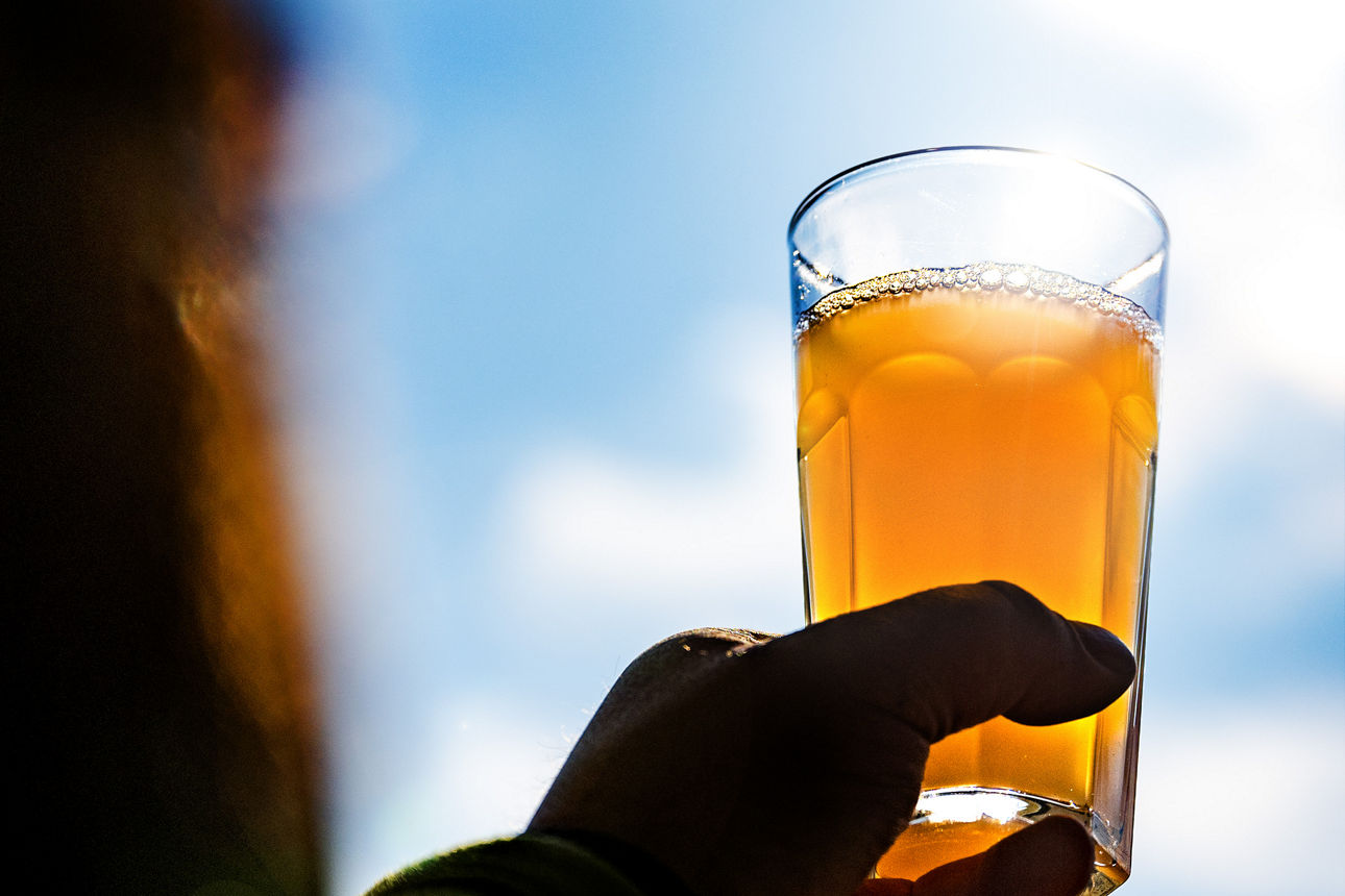 Ein Mensch hält ein Glas Apfelsaft in den Himmel