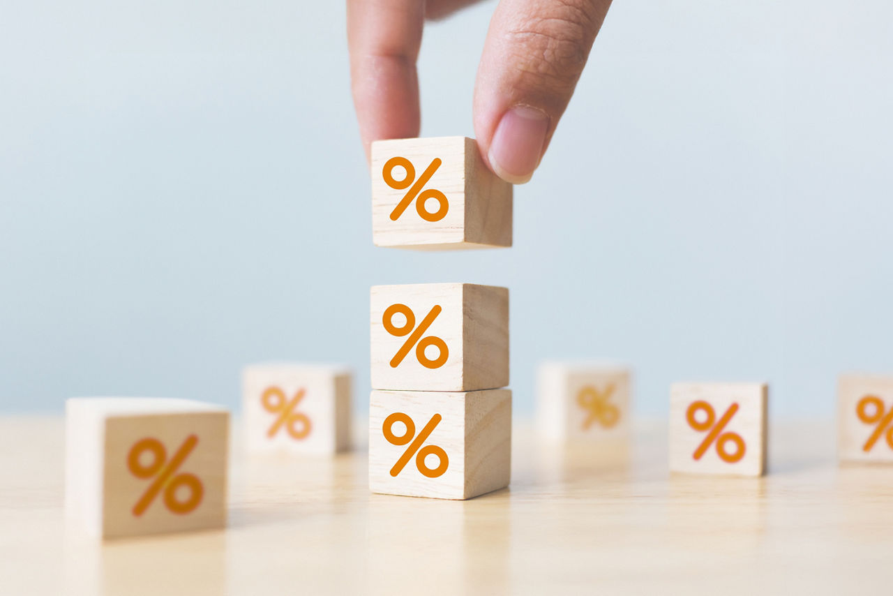 Hand stapelt Holzklötze mit orangenen Prozentzeichen auf einem hellen Untergrund.