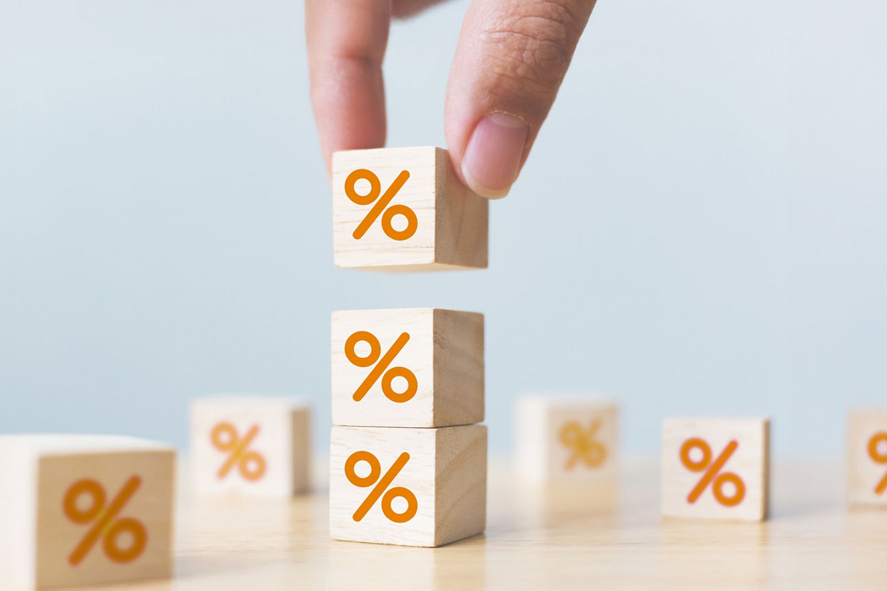 Hand stapelt Holzklötze mit orangenen Prozentzeichen auf einem hellen Untergrund.