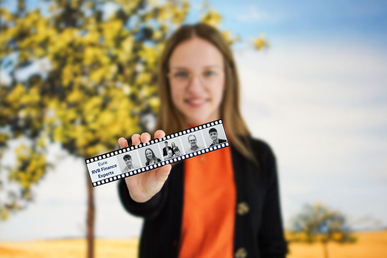 Junge Frau hält einen Filmstreifen mit Fotos junger Menschen und dem Text 'Eure RVB Finance Experts' vor einem Baum mit hellgrünen Blättern