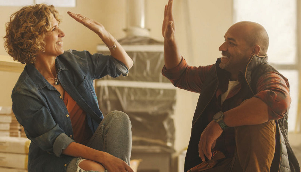 Ein Mann steht lächelnd vor einem modernisierten Haus mit Wärmepumpe.