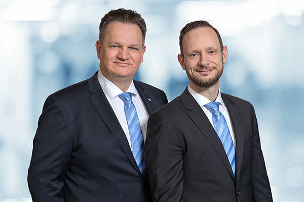 Zwei Männer in formellen Anzügen und Krawatten stehen nebeneinander