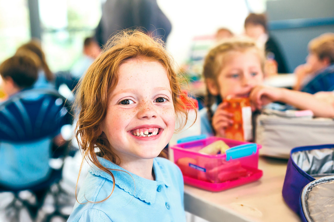 Smiling school students in uniform missing a tooth with a healthy sandwich for lunch