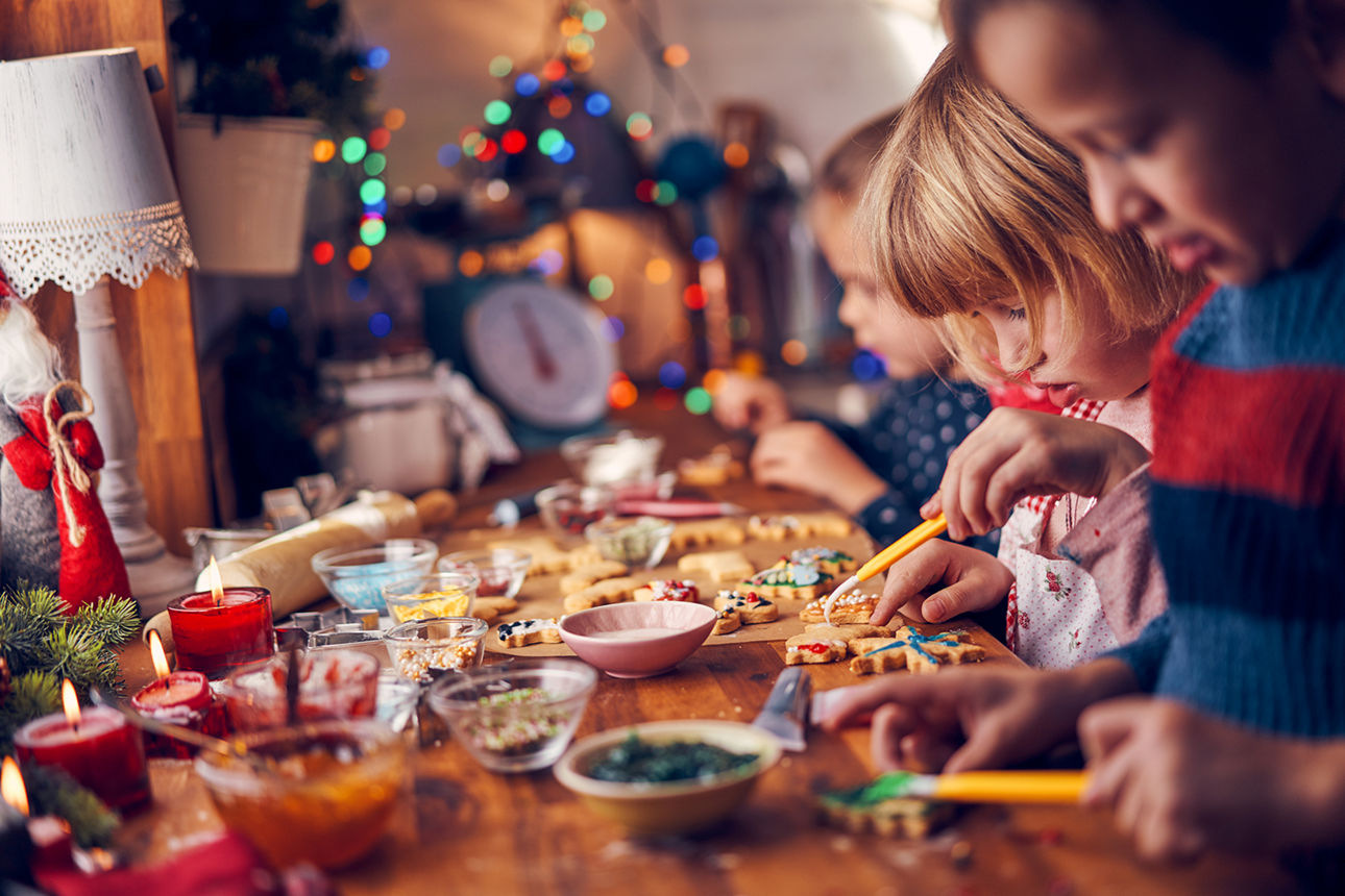 Kinder verzieren bunte Plätzchen an einem Tisch mit Schüsseln, Kerzen und Weihnachtsdeko.