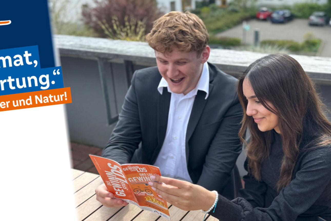 2 Azubis sitzen an einem Tisch und lesen den Gewinnsaprflyer