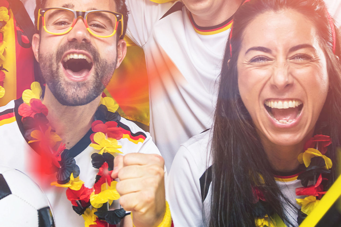 Jubelnde Fans in Schwarz-Rot-Gold mit Fußball und Fanartikeln feiern gemeinsam bei einem Fußballspiel.