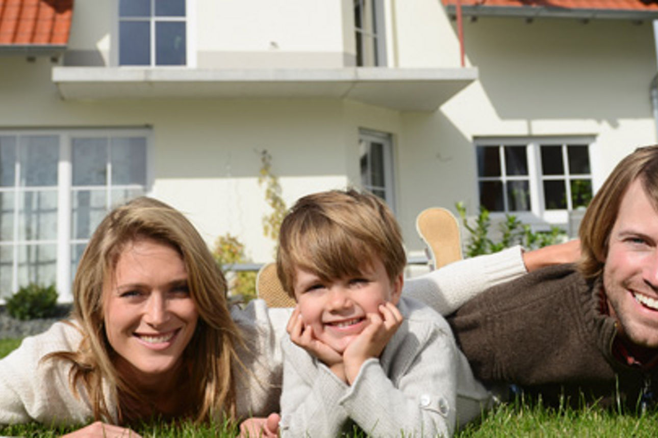 Eine vierköpfige Familie liegt im Gras vor ihrem Haus und lächelt in die Kamera.
