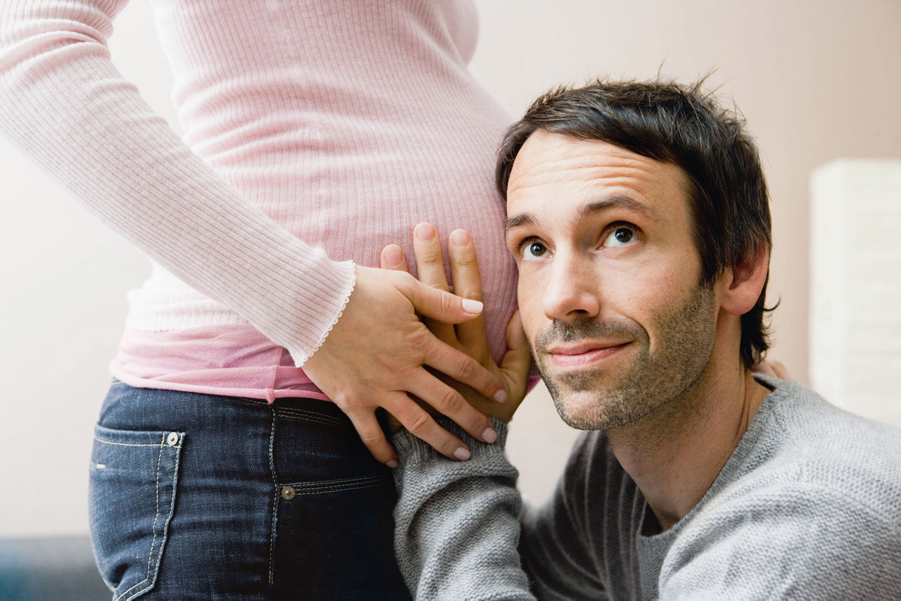 Mann horcht am Bauch einer Schwangeren