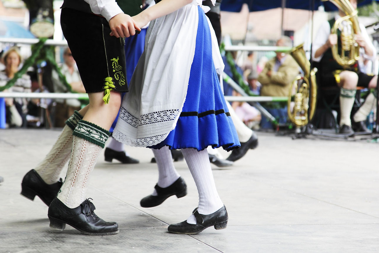 Eine Frau und ein Mann tanzen in traditionellen Trachten vor Blechblasenden.