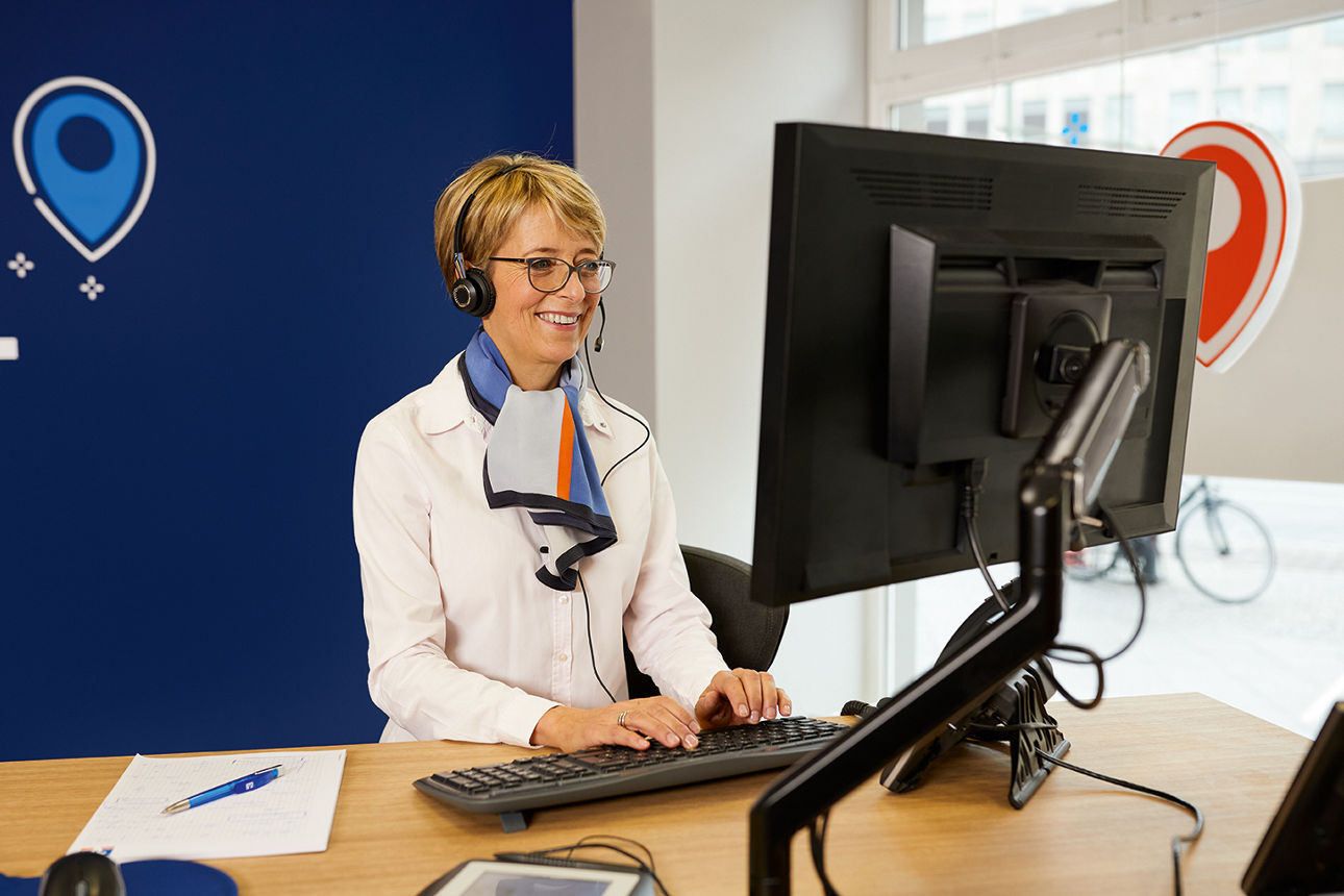 Frau steht vor einem Rechner mit einem Headset auf