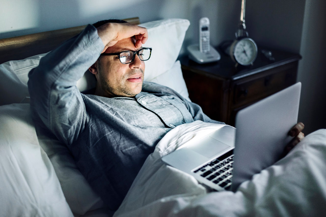 Mann liegt mit aufgeklapptem Laptop auf dem Bauch im Bett
