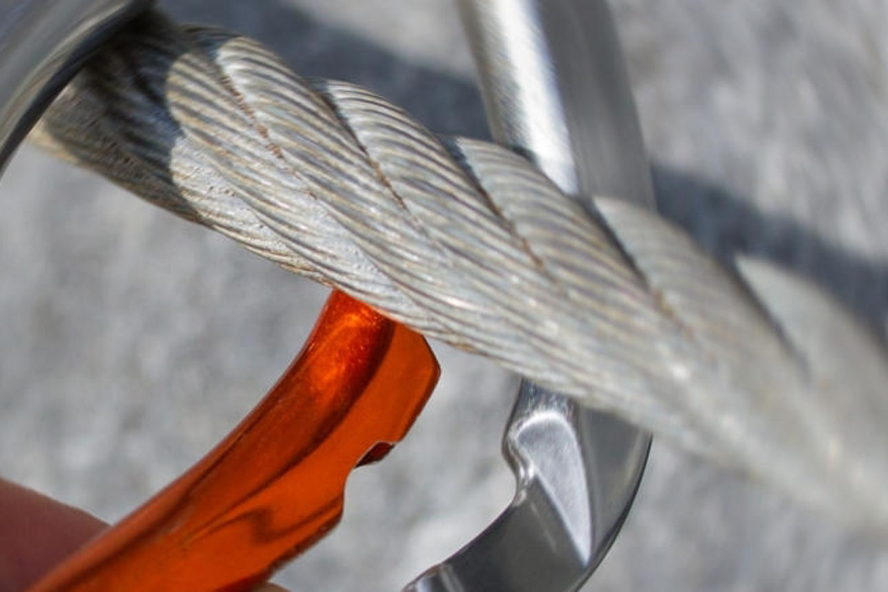 Eine Person ergreift einen Karabinerhaken, der an einem Seil befestigt ist.