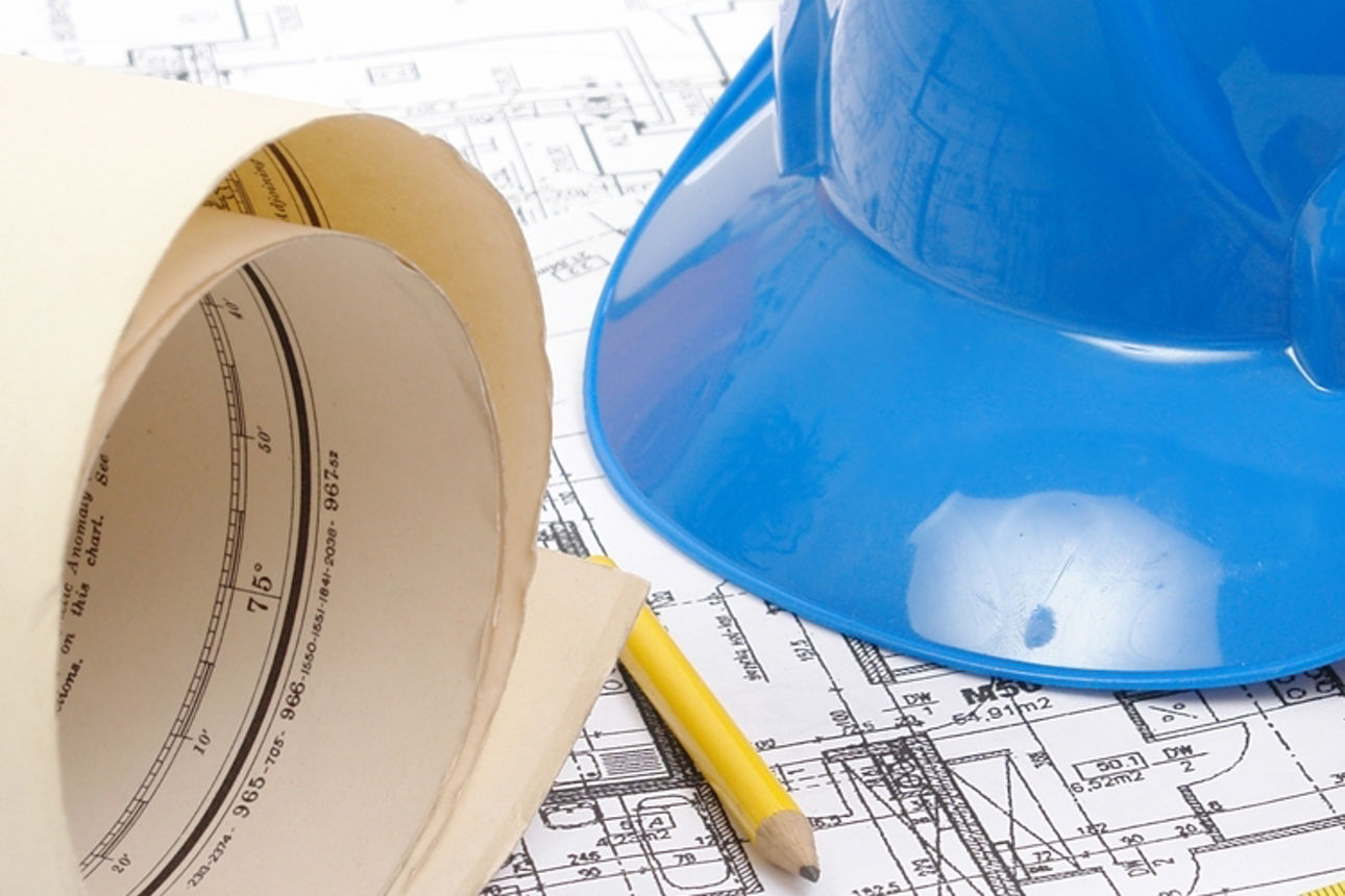 Bauwerkzeuge und ein blauer Schutzhelm liegen auf detaillierten Bauplänen