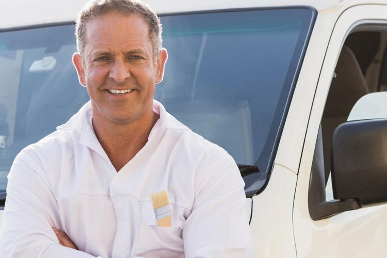 Ein Mann steht neben einem weißen Lieferwagen und blickt mit neutraler Miene in die Kamera.