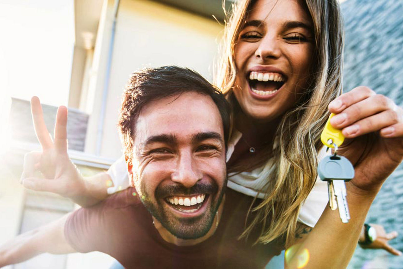 Ehepaar lacht in die Kamera und zeigt freudig ihren Schlüssel für das Eigenheim