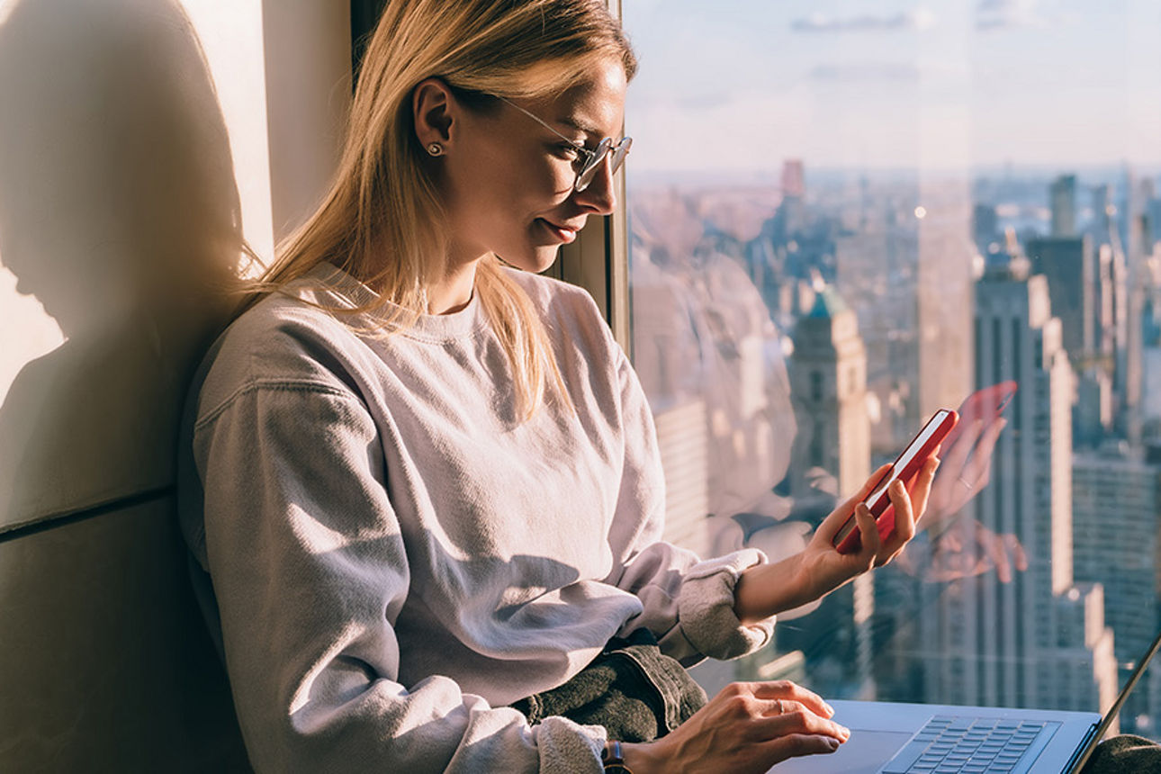 Junge Frau schaut aufs Handy, im Hintergrund die Skyline einer Großstadt