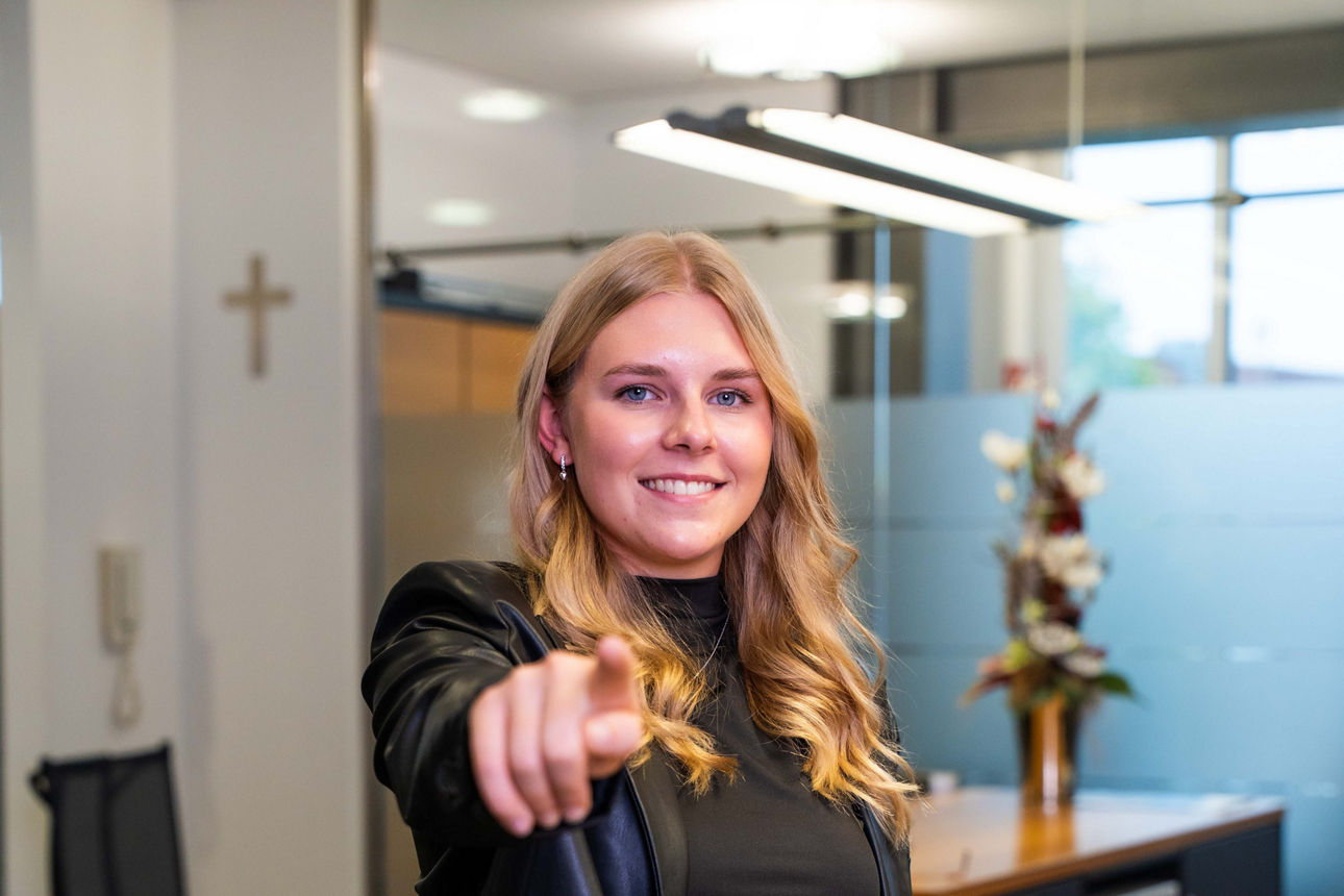 Eine junge Faru steht vor dem Bankschalter und zeigt den Finger auf dich
