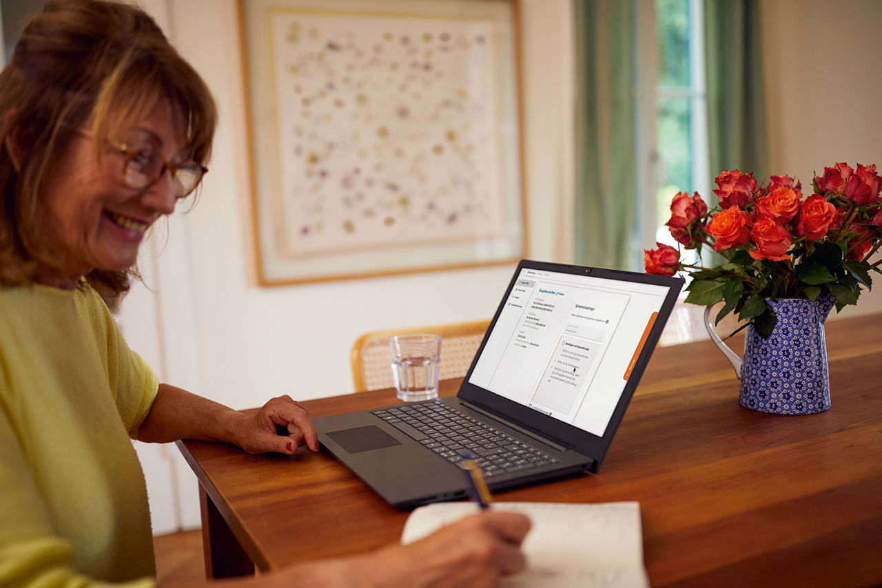 Frau schaut in einen Laptop und notiert sich etwas