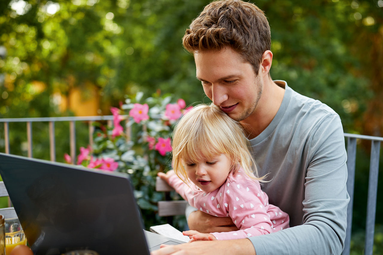 Mann sitzt mit seiner Tochter draußen und schaut auf seinen Laptop