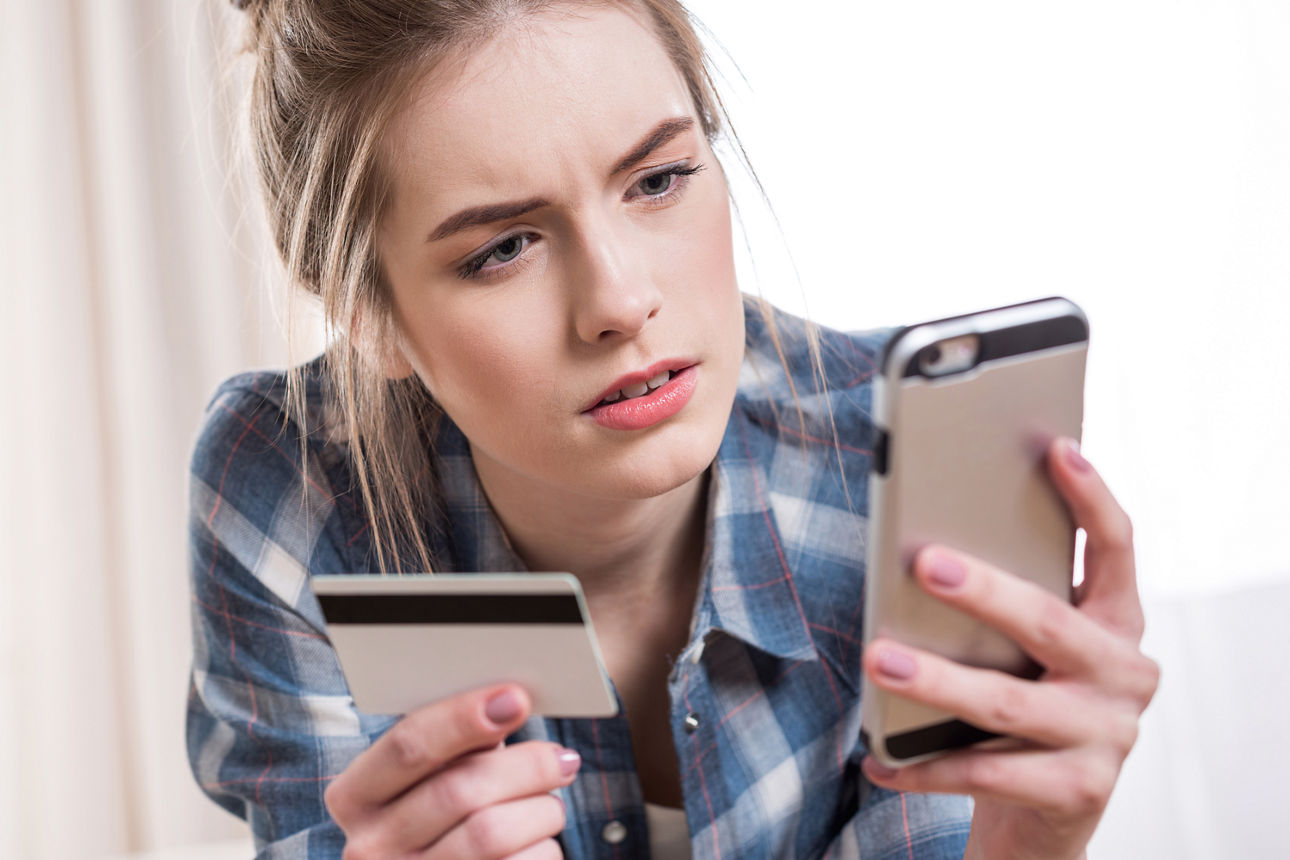 Frau mit girocard und Handy in der Hand schaut konzentriert auf ihr Handy