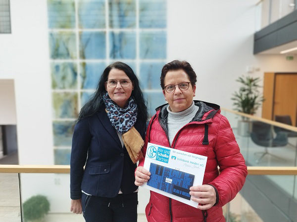 Zwei Frauen halten gemeinsam eine Urkunde in der Hand.