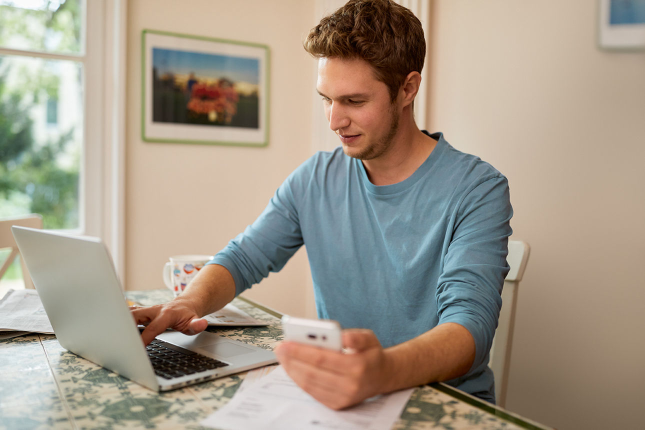 Ein Mann sitzt mit seinem Handy am Laptop und macht OnlineBanking