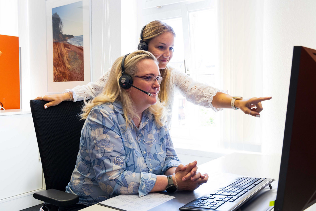 Zwei Mitarbeiter:innen der Telefonfiliale mit Headset vor einem Bildschirm