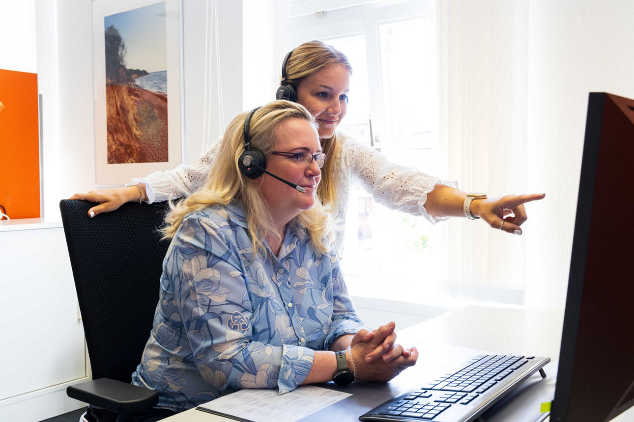 Zwei Mitarbeiter:innen der Telefonfiliale mit Headset vor einem Bildschirm
