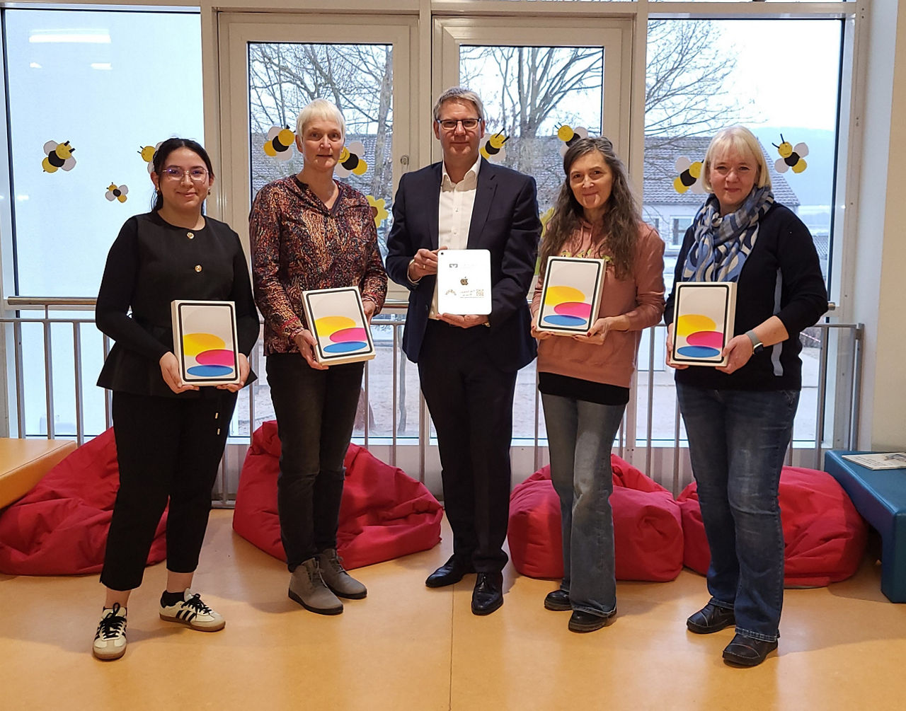 Gruppenfoto von fünf Personen, die in einem Innenraum stehen und jeweils ein Tablet-Gerät in der Hand halten