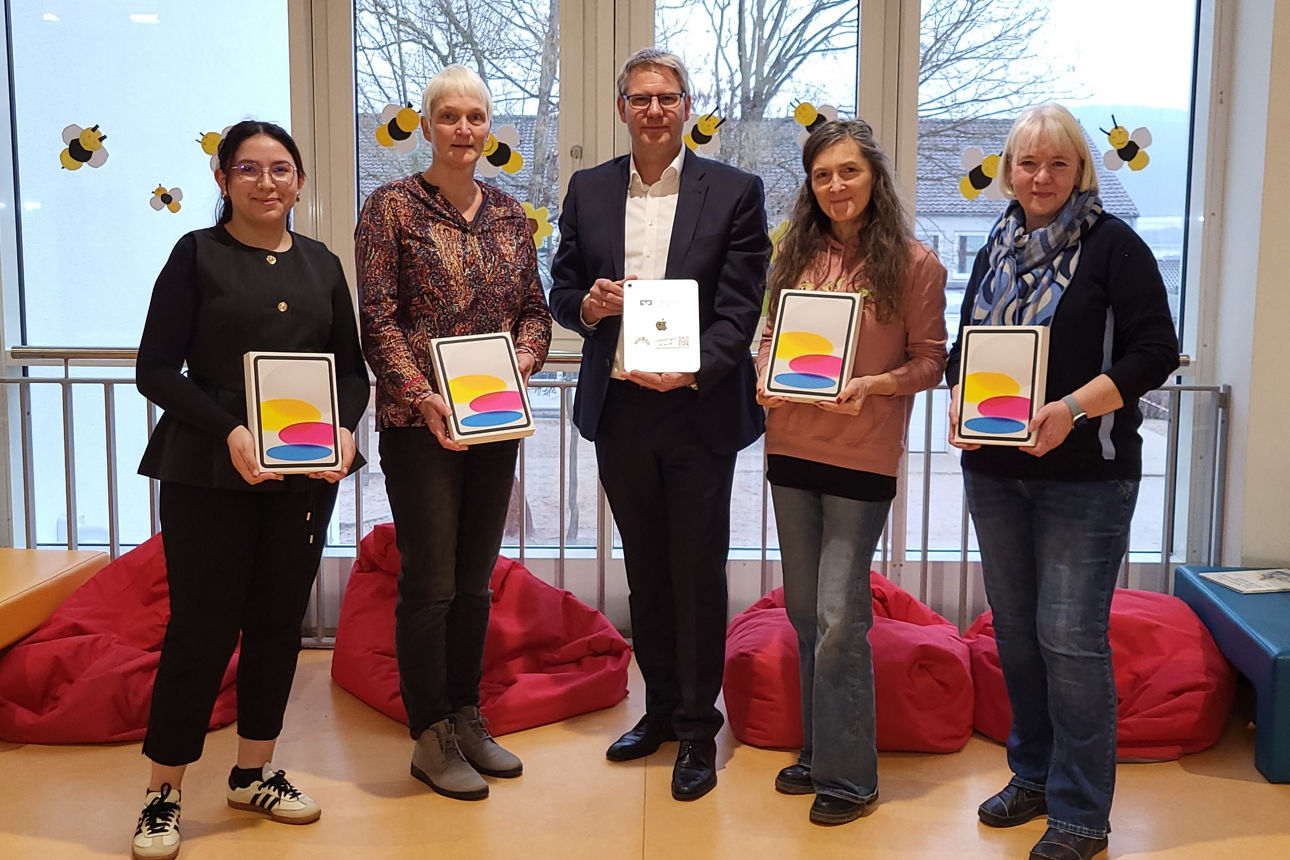 Gruppenfoto von fünf Personen, die in einem Innenraum stehen und jeweils ein Tablet-Gerät in der Hand halten