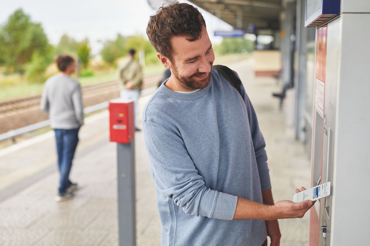 Mann bezahlt auf einem Bahnsteig am Ticketautomaten mit dem Handy 