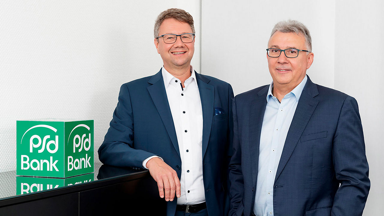 Foto unserer Vorstände Lothar Angermair und Martin Schöndorf in einem Büro mit PSD Bank Logo