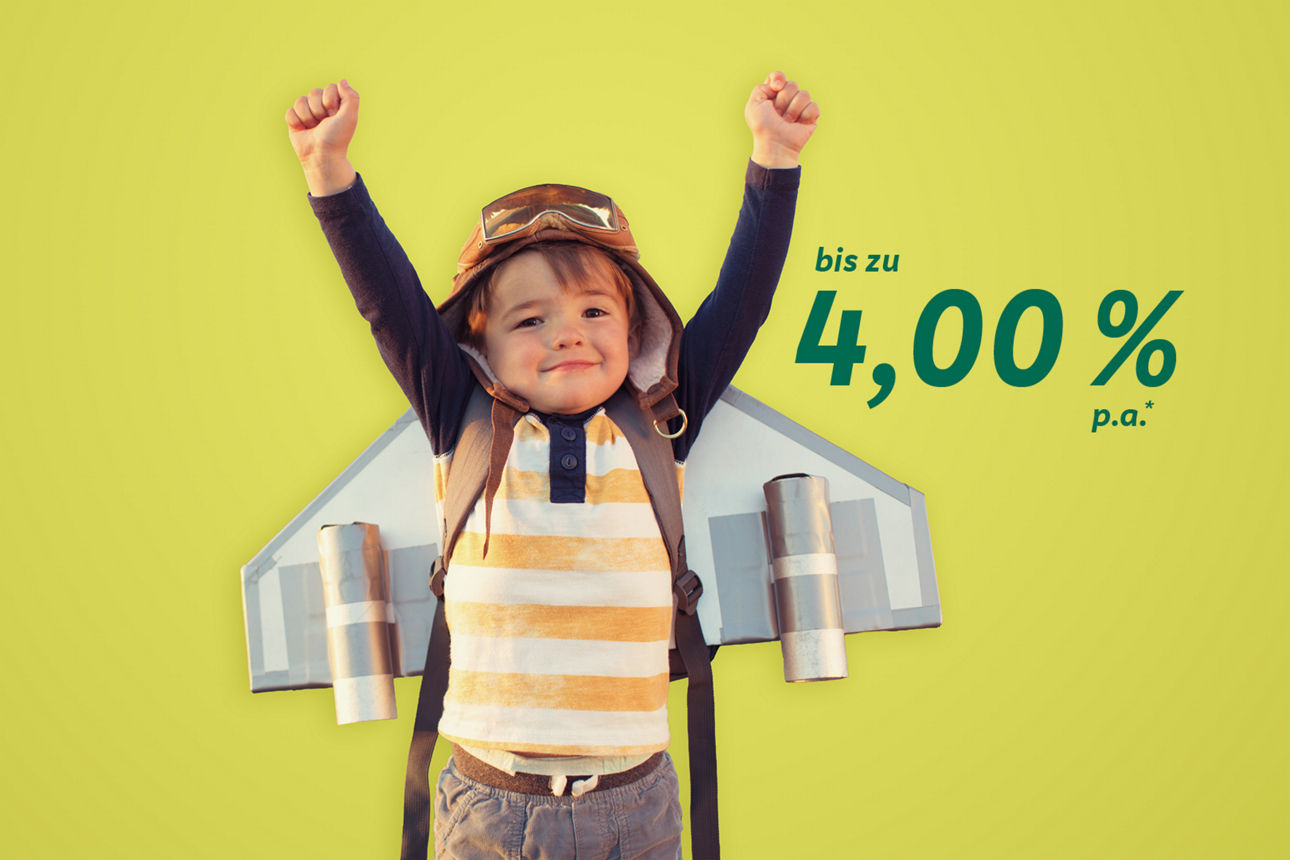 Ein kleiner Junge steht mit gebastelten Flügeln auf dem Rücken da und streckt die Hände in die Höhe.