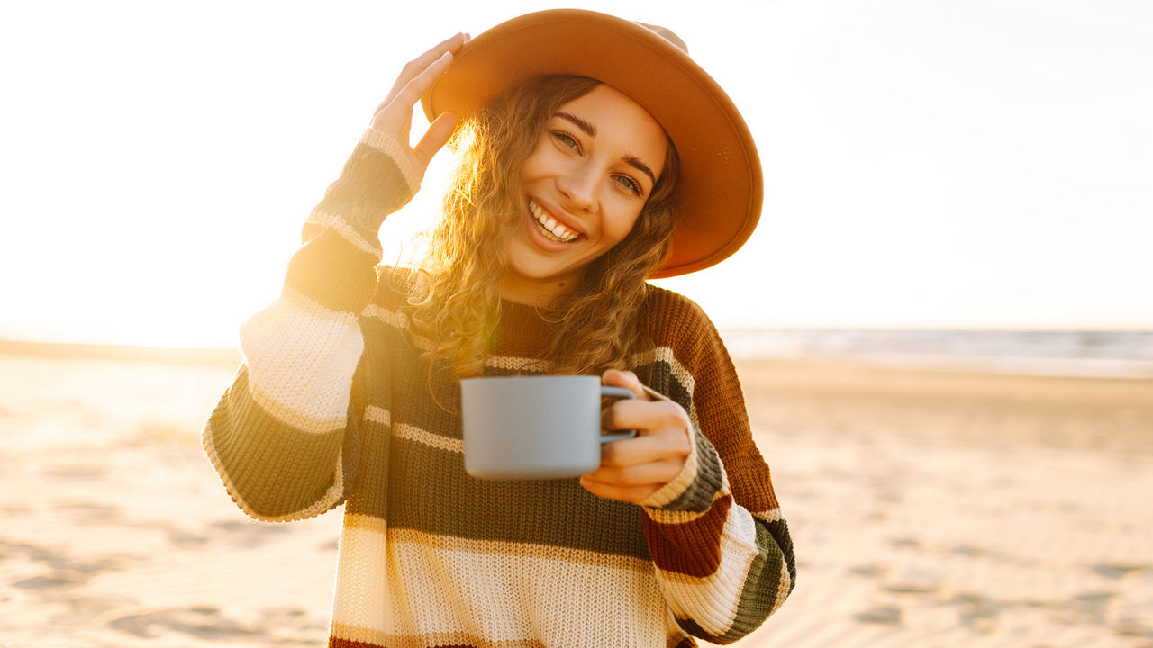 Junge Frau trinkt Morgenkaffee bei einem Picknick am Strand. 