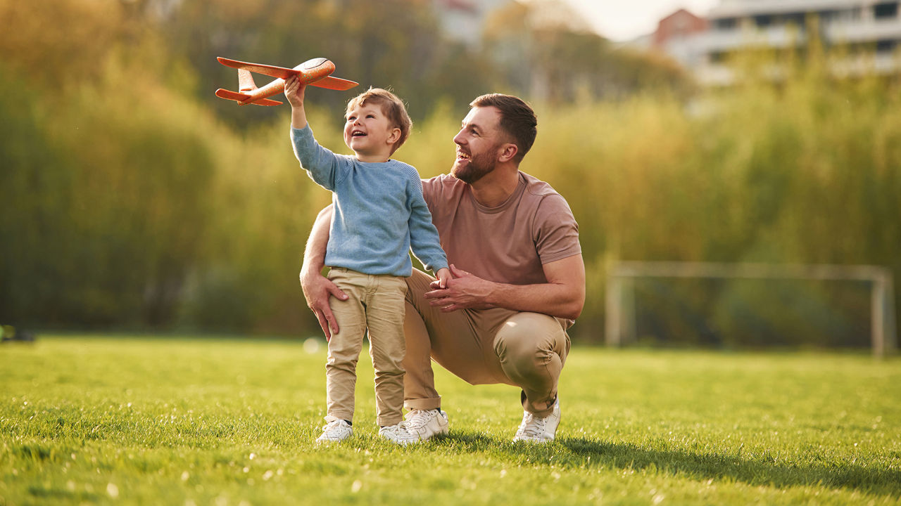 Weekend activities. Playing with toy plane. Happy father with son are having fun on the field at summertime.