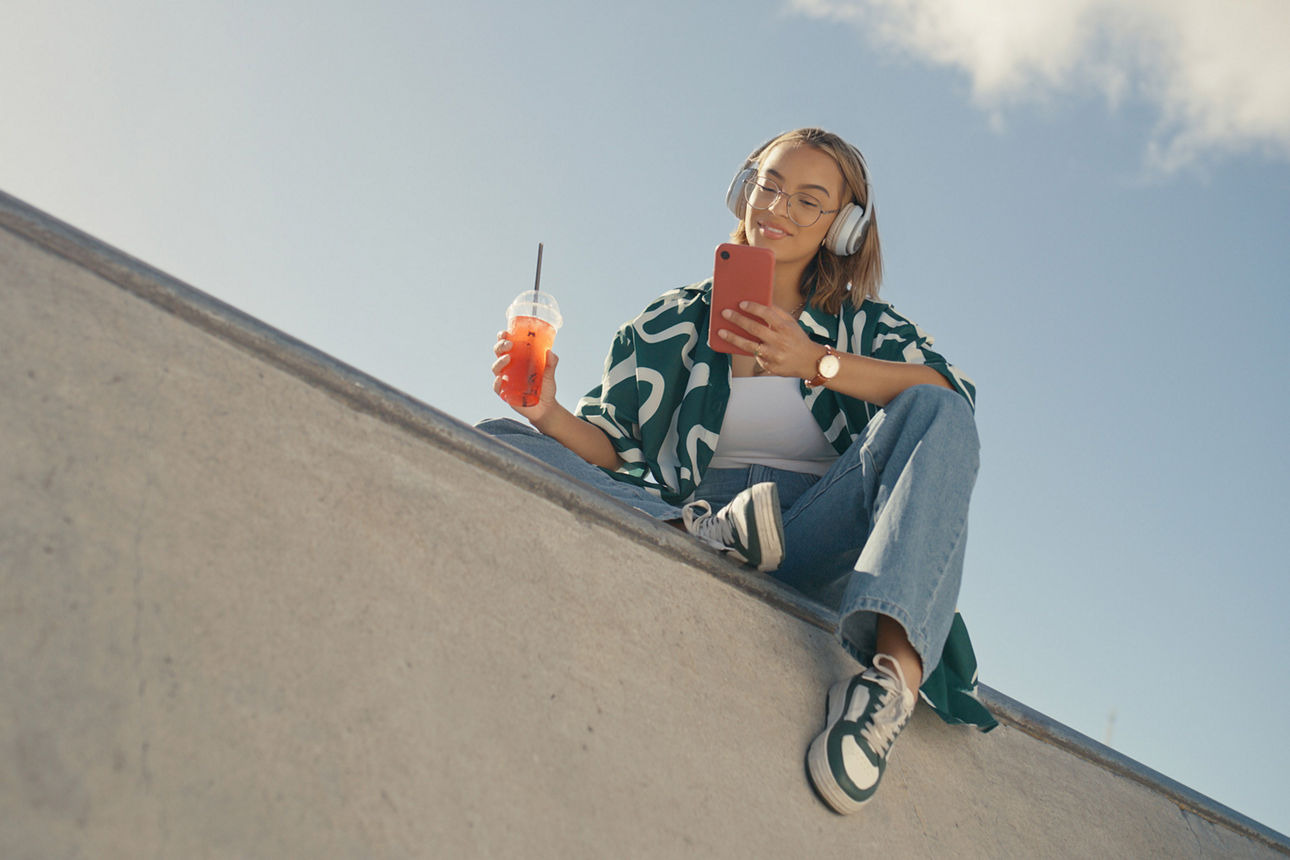 Eine Frau sitzt auf einer Wand mit einem Cocktail und einem Handy in der Hand