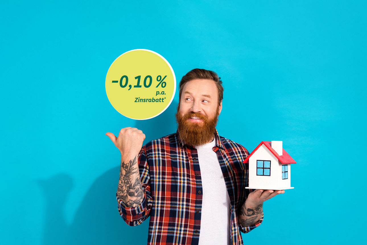 Ein Mann hält ein Haus in einer Hand und mit einer anderen Hand zeigt auf den Zinsrabatt (Minus 0,10 % p.a.)