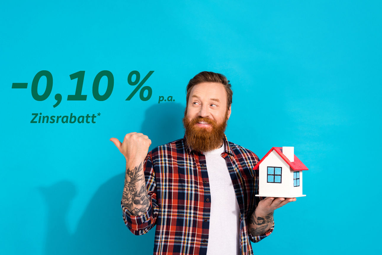 Ein Mann hält ein kleines Haus in der rechten Hand und zeigt mit der linken Hand auf einen Zinsrabatt von - 0,10 %.