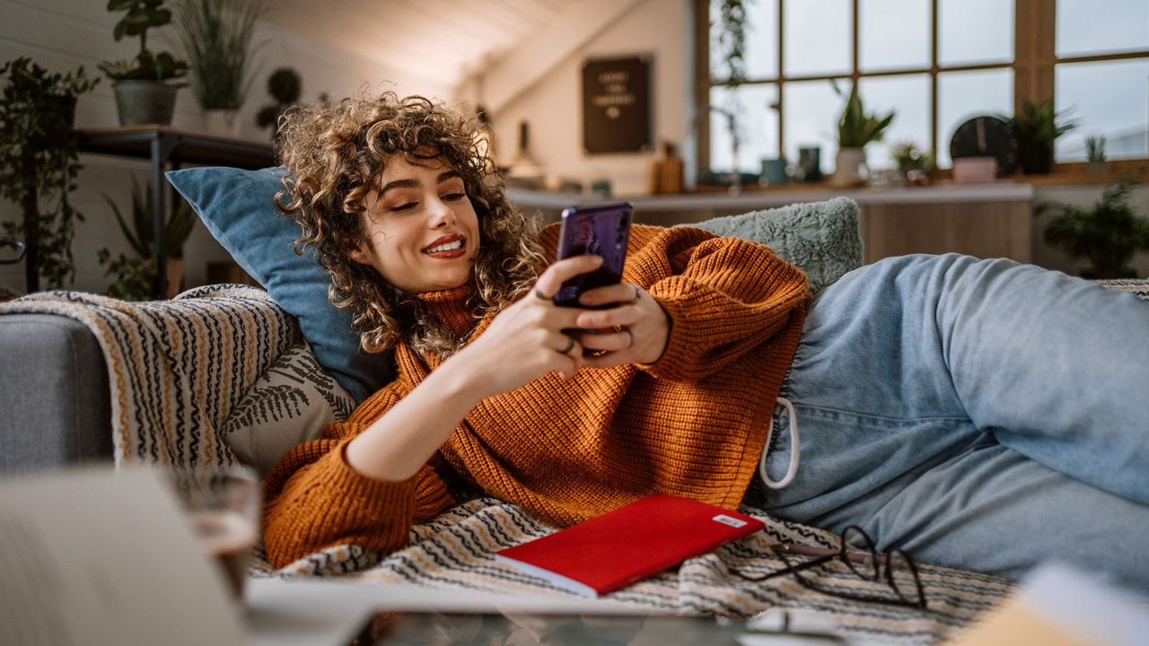 Eine junge Frau liegt auf einem Sofa mit einem Handy in der Hand