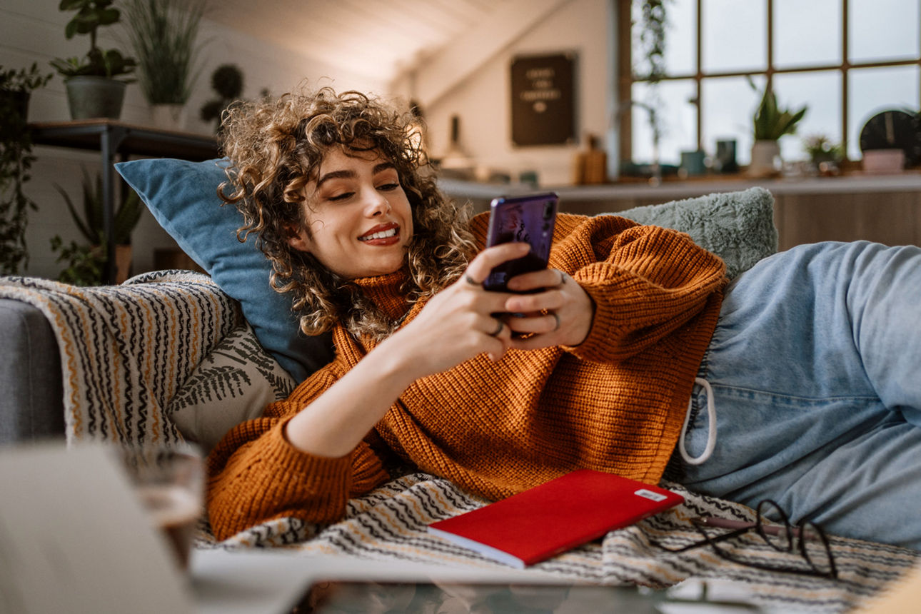 Eine junge Frau liegt auf einem Sofa mit einem Handy in der Hand