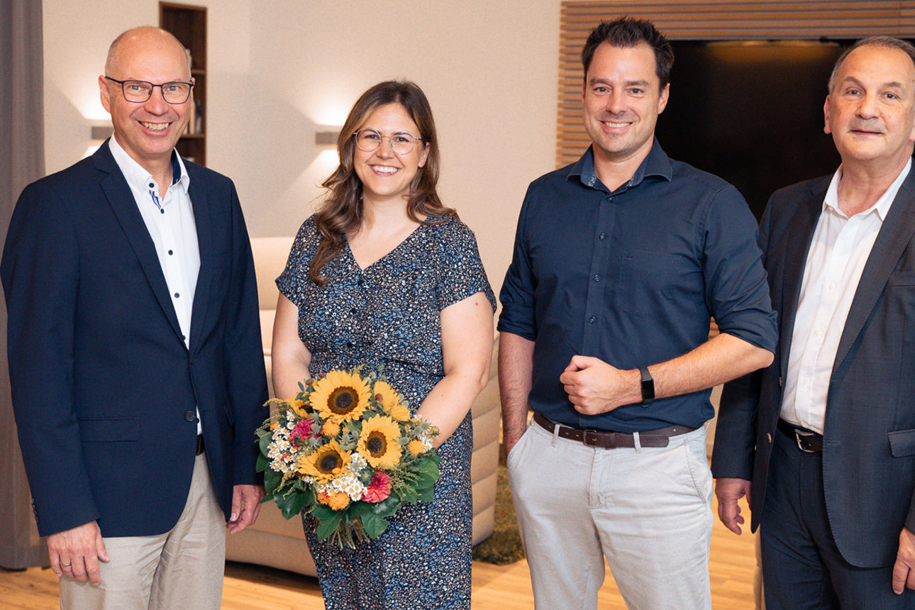 Vier Personen, die lächelnd in die Kamera schauen. Der Frau im Foto hat ein Stipendium und einen Blumenstrauß erhalten.