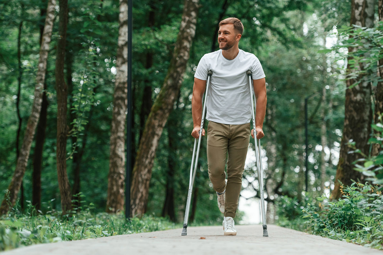 Ein Mann mit Krücken macht einen Spaziergang im Wald.