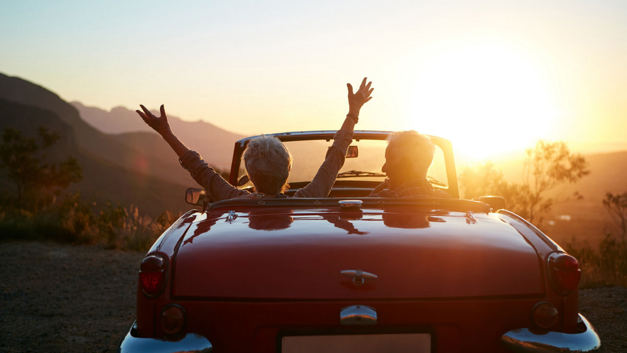 Ein Paar sitzt in einem Cabrio und schaut sich den Sonnenuntergang an. 